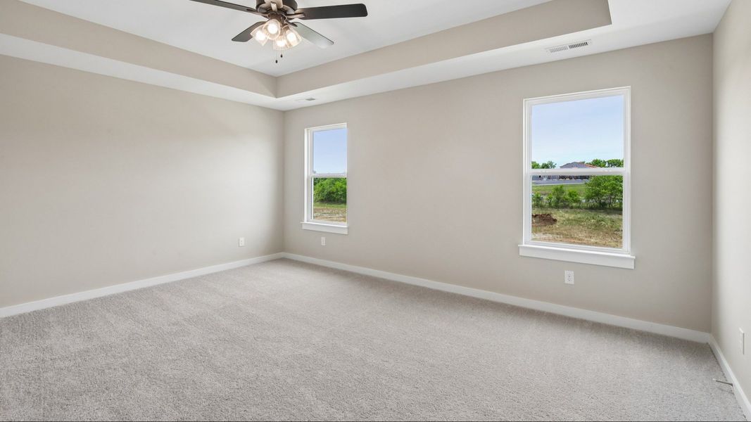 Bedroom with tray ceiling, windows, and ceiling fan