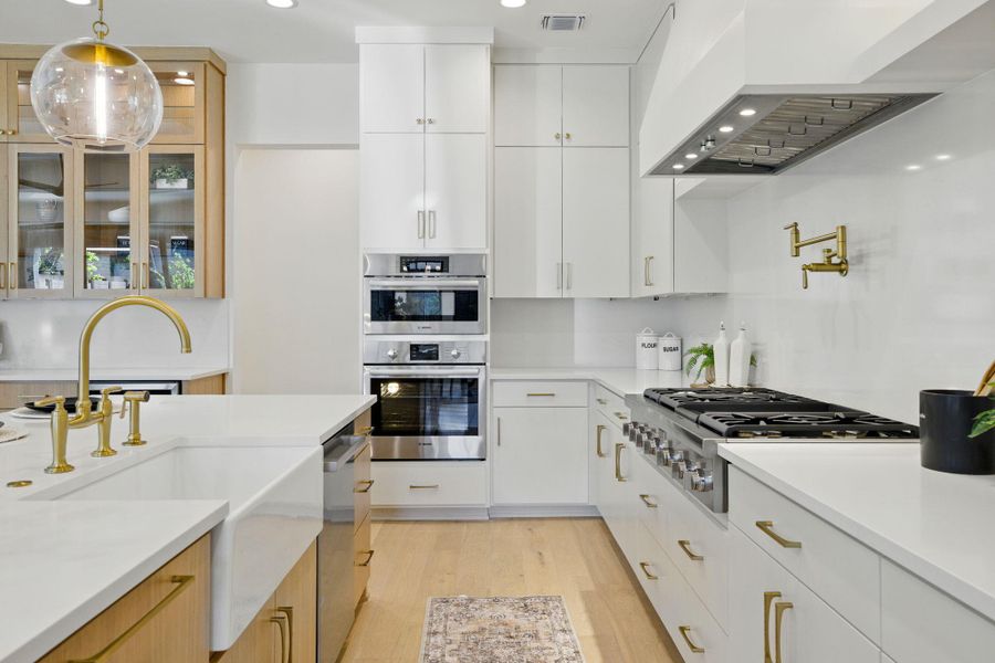 Kitchen featuring appliances with stainless steel finishes, a sink, wall chimney range hood, light wood-style flooring, and light countertops