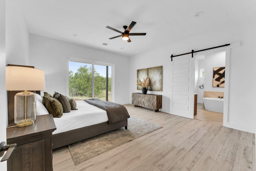 A spacious bedroom provides a tranquil retreat with wide plank flooring, a ceiling fan, and large windows revealing verdant outdoor scenery. A spacious bedroom provides a tranquil retreat with wide plank flooring, a ceiling fan, and large windows revealing verdant outdoor scenery.