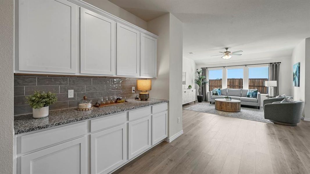 Kitchen with white cabinets, light stone counters, light wood finished floors, open floor plan, and decorative backsplash