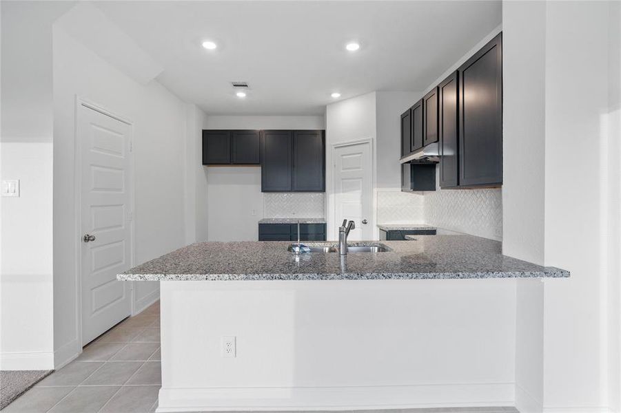 This spacious kitchen features high ceilings, stained wood cabinets, granite countertops, SS appliances, modern tile backsplash, recessed lighting, extended countertop for breakfast bar, and pantry all overlooking your huge family room