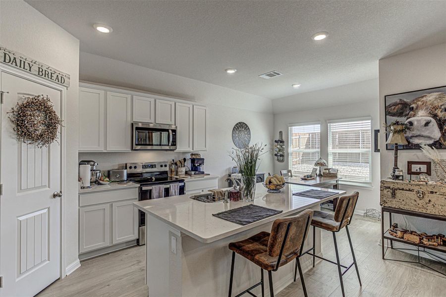 Kitchen featuring white cabinetry, stainless steel appliances, a kitchen island with sink, a kitchen breakfast bar, and light stone countertops