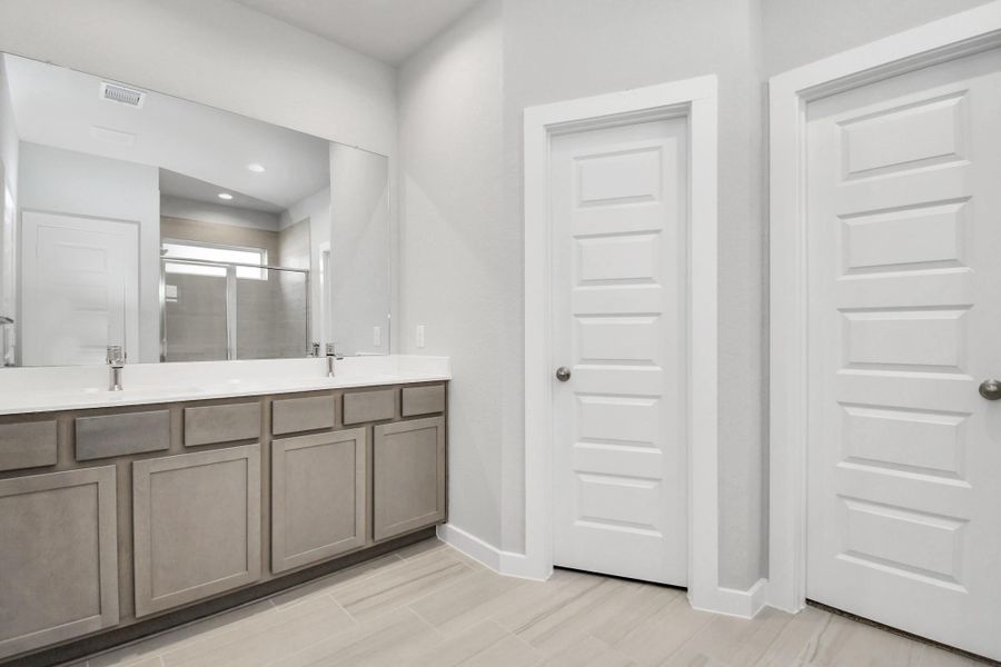Immerse yourself in a luxurious retreat within the confines of your main bathroom and elevate your daily routine at the refined vanity, now boasting double sinks, light-toned countertops, modern hardware, and captivating bright recessed lights. Sample photo of completed home with similar floor plan. Actual colors and selections may vary.