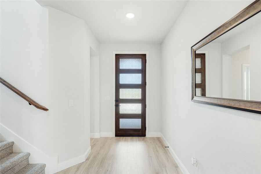 Entryway with dark wood front door with glass panels, light hardwood floors, staircase, and wall mirror.