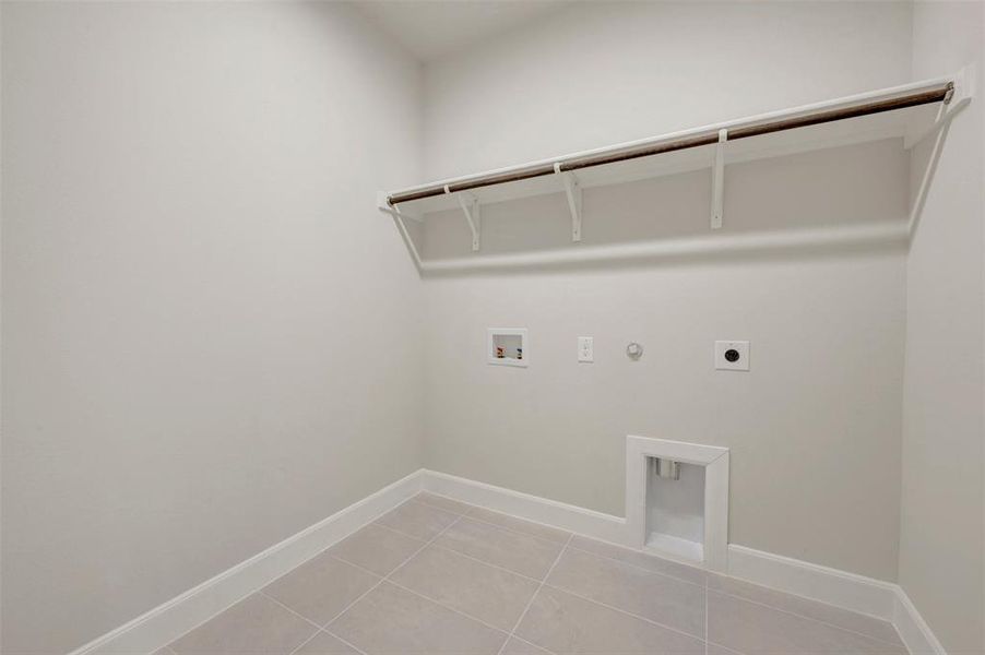 Dedicated utility room featuring light gray tile flooring, white baseboards, and a built-in shelf with a hanging rod