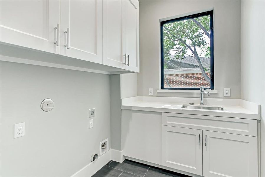 Large upstairs utility room with abundance of cabinetry, sink and large window.