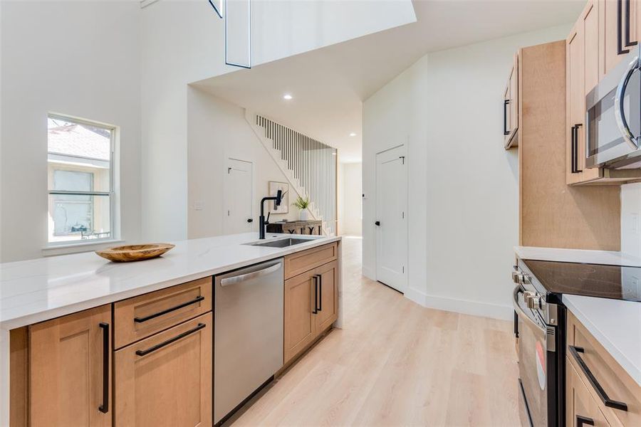 Kitchen with light stone countertops, sink, stainless steel appliances, and light wood-type flooring