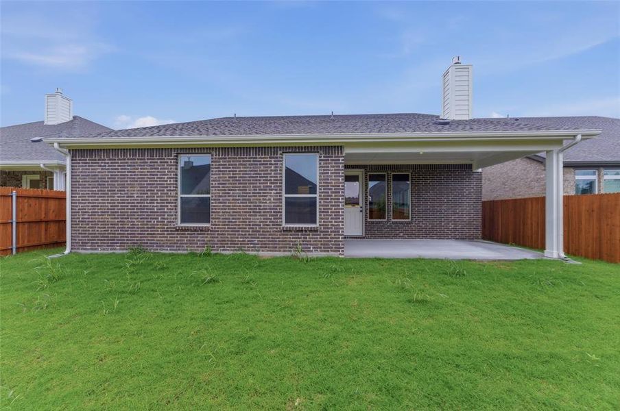 Expansive backyard featuring a covered patio with concrete flooring, dark brick exterior, and a wooden privacy fence