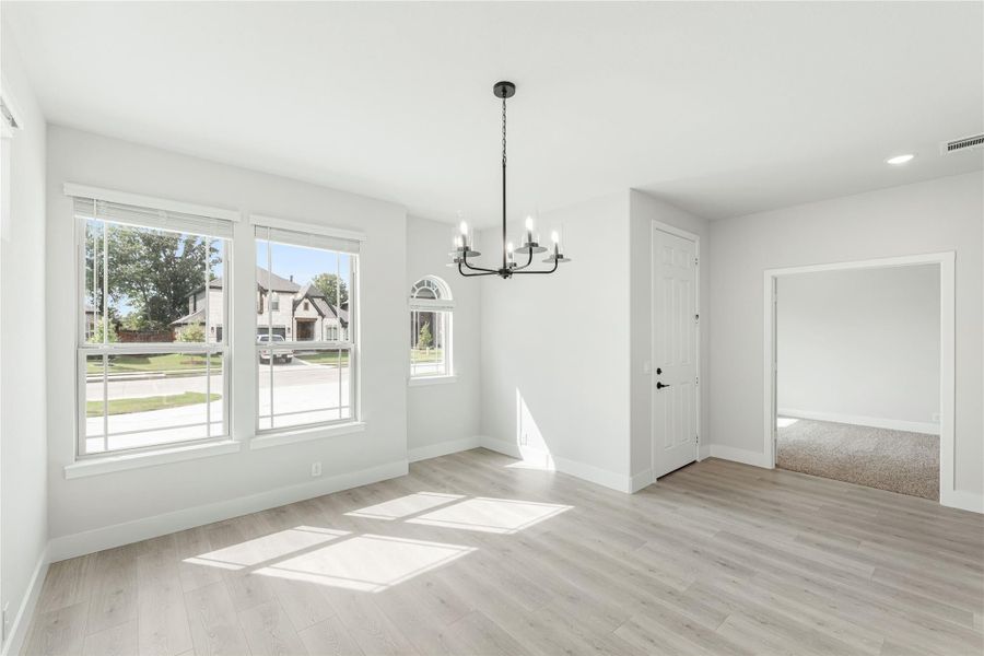 Empty dining room with light wood floors, black chandelier, and large windows with natural light