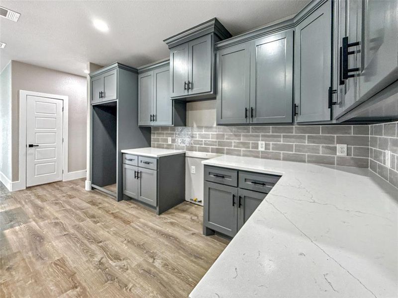 Kitchen with gray cabinets, light stone counters, decorative backsplash, light wood-style floors, and recessed lighting