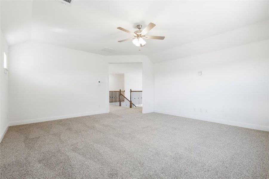 Carpeted empty room with lofted ceiling and a ceiling fan Carpeted empty room with lofted ceiling and a ceiling fan