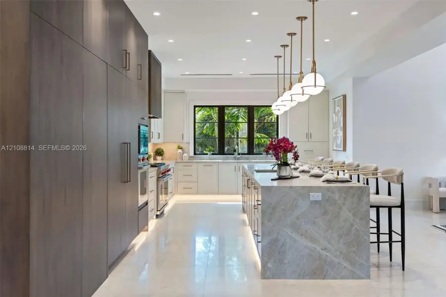 Kitchen featuring floor-to-ceiling cabinetry, a waterfall-edge stone island, recessed ceiling lighting, a row of spherical pendant lights, and large-format tile flooring Kitchen featuring floor-to-ceiling cabinetry, a waterfall-edge stone island, recessed ceiling lighting, a row of spherical pendant lights, and large-format tile flooring