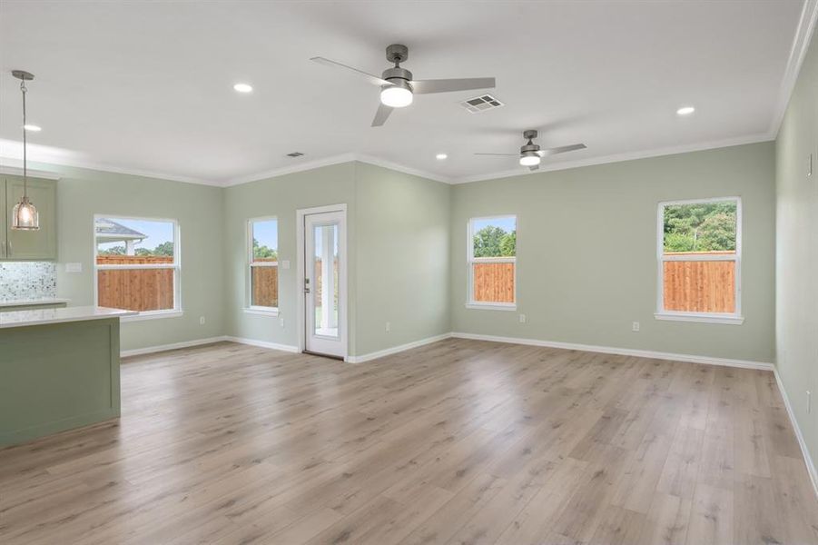 Unfurnished living room featuring light hardwood / wood-style flooring, ceiling fan, plenty of natural light, and crown molding