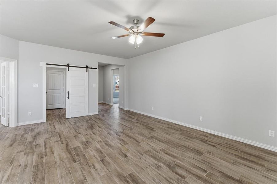 Unfurnished bedroom with a barn door, light wood-style flooring, and ceiling fan