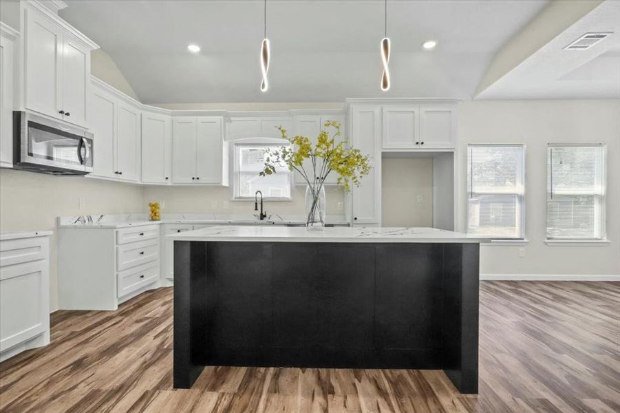 Kitchen with light wood finished floors, stainless steel microwave, white cabinetry, a center island, and recessed lighting Kitchen with light wood finished floors, stainless steel microwave, white cabinetry, a center island, and recessed lighting