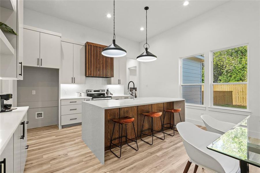 Kitchen with light stone counters, a breakfast bar, light wood-style floors, a kitchen island with sink, and backsplash