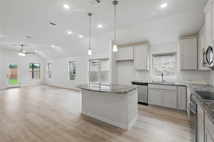 Kitchen with dark stone countertops, lofted ceiling, decorative backsplash, stainless steel appliances, and a kitchen island