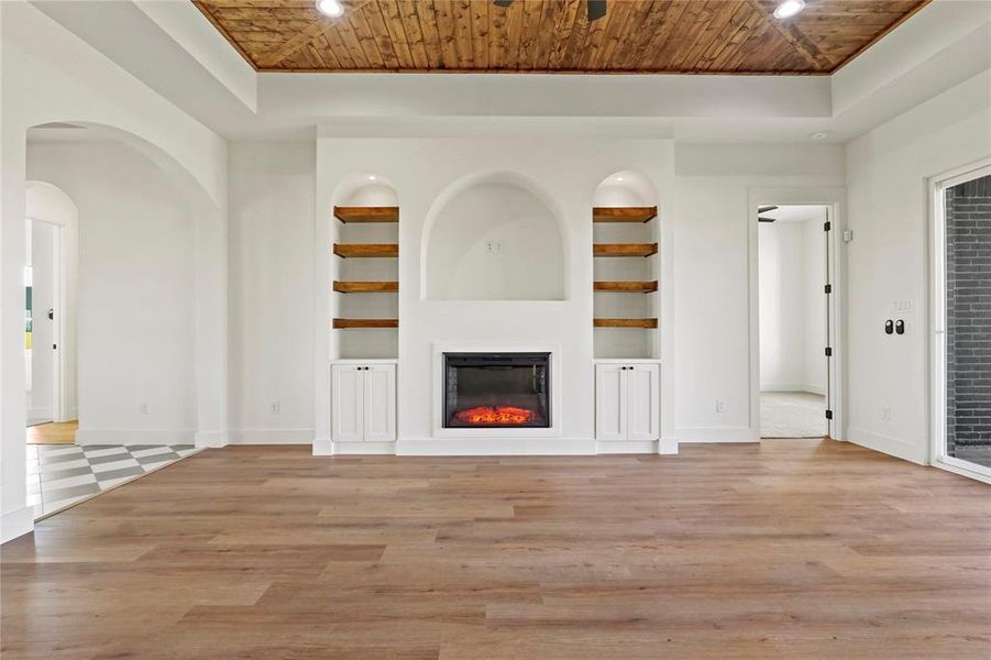 Unfurnished living room featuring built in features, wooden ceiling, light wood finished floors, a glass covered fireplace, and recessed lighting Unfurnished living room featuring built in features, wooden ceiling, light wood finished floors, a glass covered fireplace, and recessed lighting