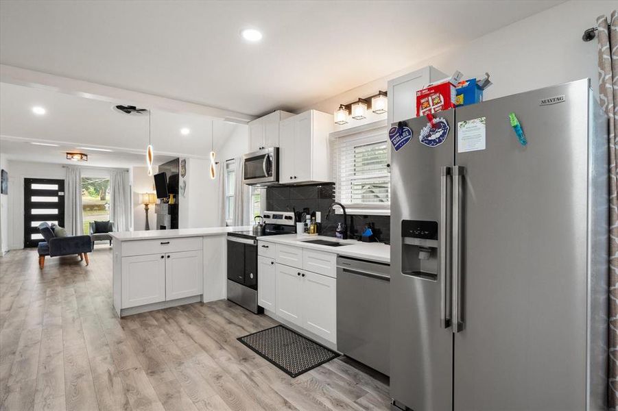 Kitchen with stainless steel appliances, a peninsula, decorative backsplash, light wood-style flooring, and white cabinets Kitchen with stainless steel appliances, a peninsula, decorative backsplash, light wood-style flooring, and white cabinets