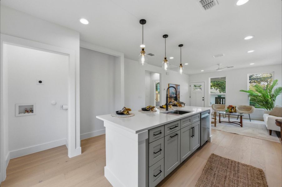 Kitchen with gray cabinets, light wood-type flooring, a center island with sink, recessed lighting, and decorative light fixtures
