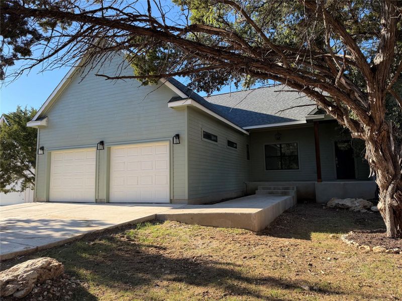 View of side of home featuring driveway, roof with shingles, a garage, and a patio View of side of home featuring driveway, roof with shingles, a garage, and a patio