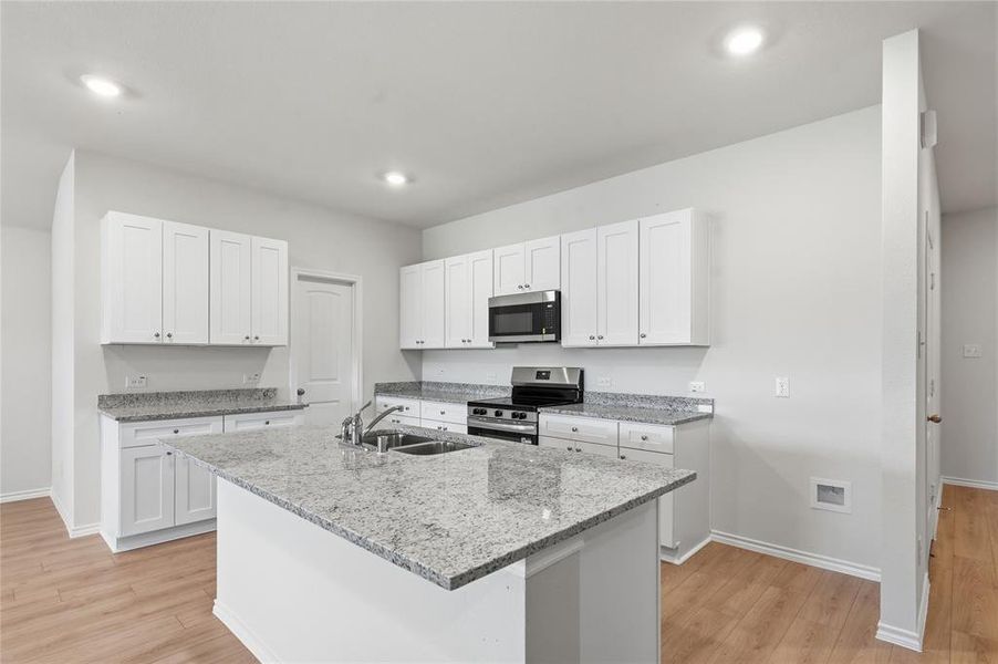 Kitchen featuring a central island with an undermount sink, white cabinetry, granite countertops, stainless steel appliances, and wood-finish flooring