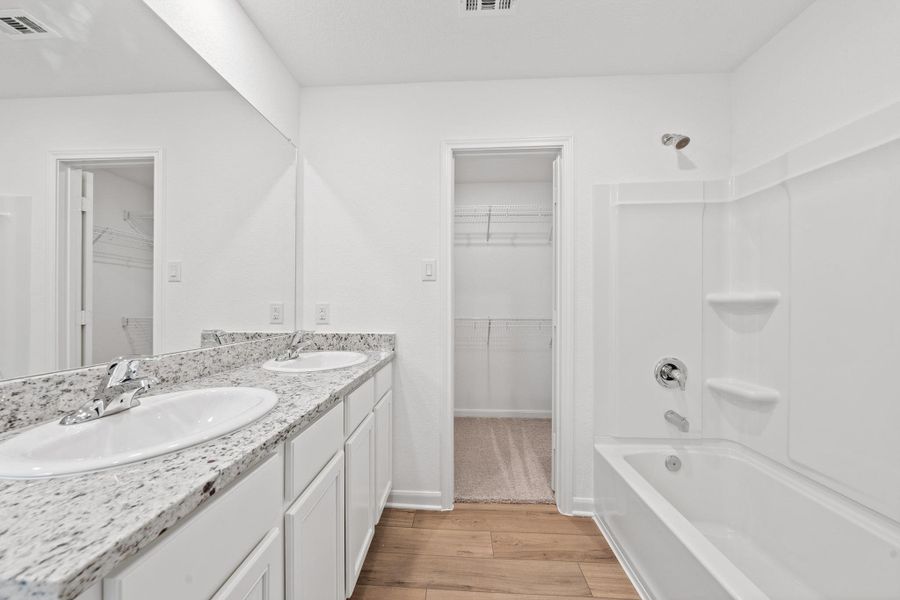 Full bath featuring a spacious closet, light wood-style flooring, double vanity, and shower / bathtub combination