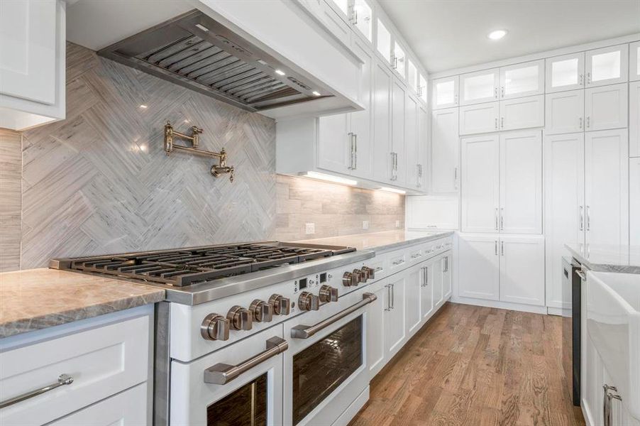 Kitchen featuring white cabinets, decorative backsplash, stainless steel stove, and custom exhaust hood