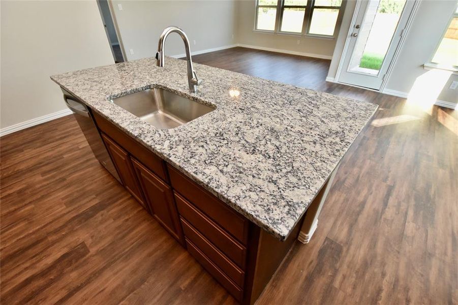 Kitchen featuring dark wood-style flooring, a kitchen island with sink, light stone counters, and open floor plan