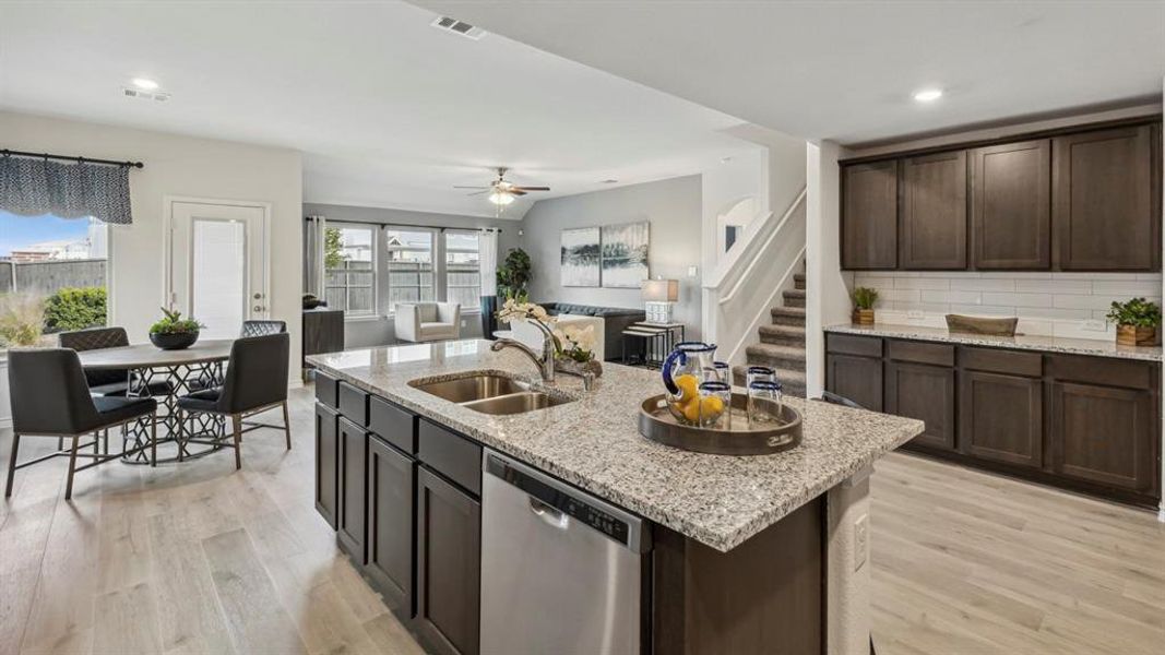 Open-concept living space featuring light wood-style flooring, a kitchen island with a double sink and granite countertops, dark wood cabinetry, and recessed lighting