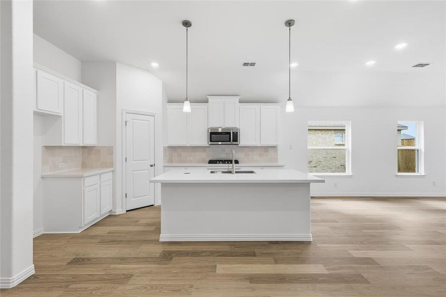 Open-concept kitchen featuring white cabinetry, a central island with sink, stainless steel microwave, and wood-finish flooring