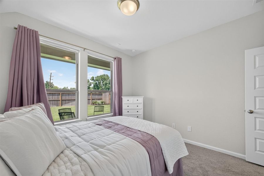 This bedroom features soft, neutral walls and a cozy carpet. Large windows with purple curtains offer plenty of natural light and a view of the backyard. The space is currently, simply furnished with a bed and a white dresser, creating a serene and inviting atmosphere. This bedroom features soft, neutral walls and a cozy carpet. Large windows with purple curtains offer plenty of natural light and a view of the backyard. The space is currently, simply furnished with a bed and a white dresser, creating a serene and inviting atmosphere.