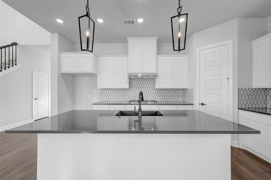 Kitchen featuring dark wood-style flooring, a kitchen island with sink, backsplash, white cabinetry, and dark stone countertops Kitchen featuring dark wood-style flooring, a kitchen island with sink, backsplash, white cabinetry, and dark stone countertops