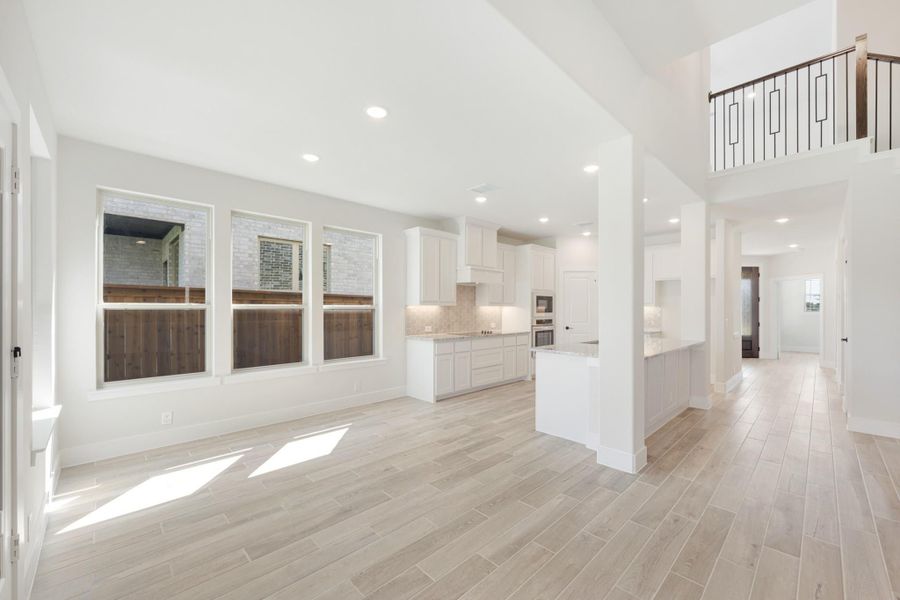 Open-concept living area with white kitchen, light wood-look tile floors, and second-floor balcony railing visible above.