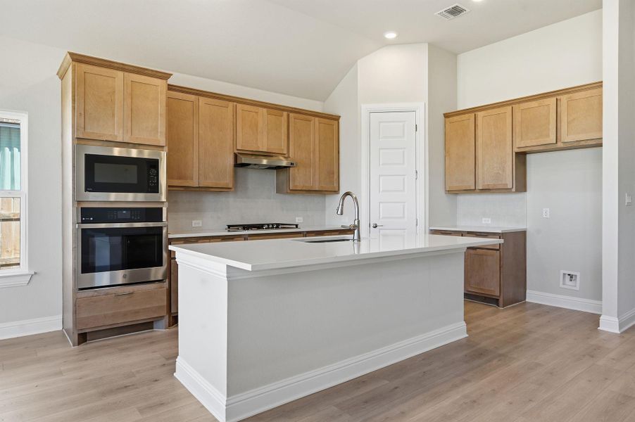 Kitchen featuring oven, built in microwave, a center island with sink, light wood-type flooring, and light stone countertops Kitchen featuring oven, built in microwave, a center island with sink, light wood-type flooring, and light stone countertops