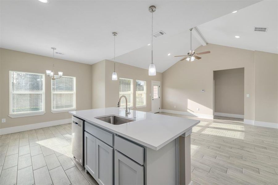 Kitchen with gray cabinetry, sink, dishwasher, vaulted ceiling with beams, and an island with sink