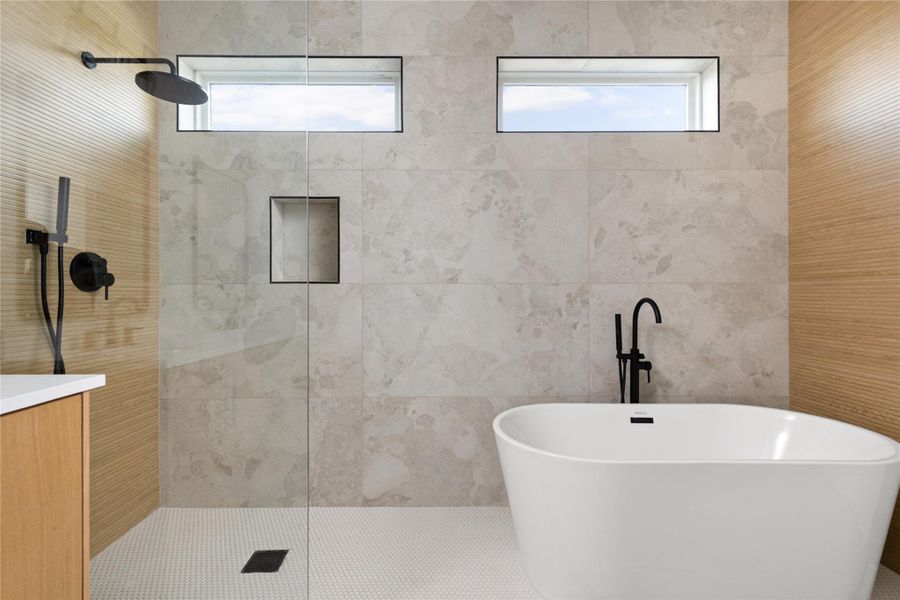 High windows invite natural light into a modern wet room featuring textured tile walls.