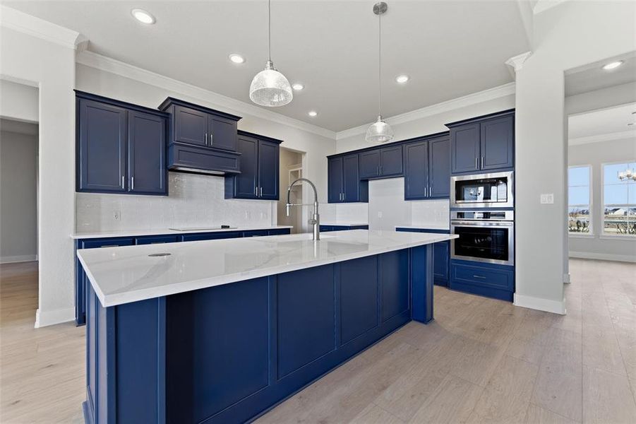 Kitchen featuring ornamental molding, decorative backsplash, stainless steel appliances, a kitchen island with sink, and light stone counters