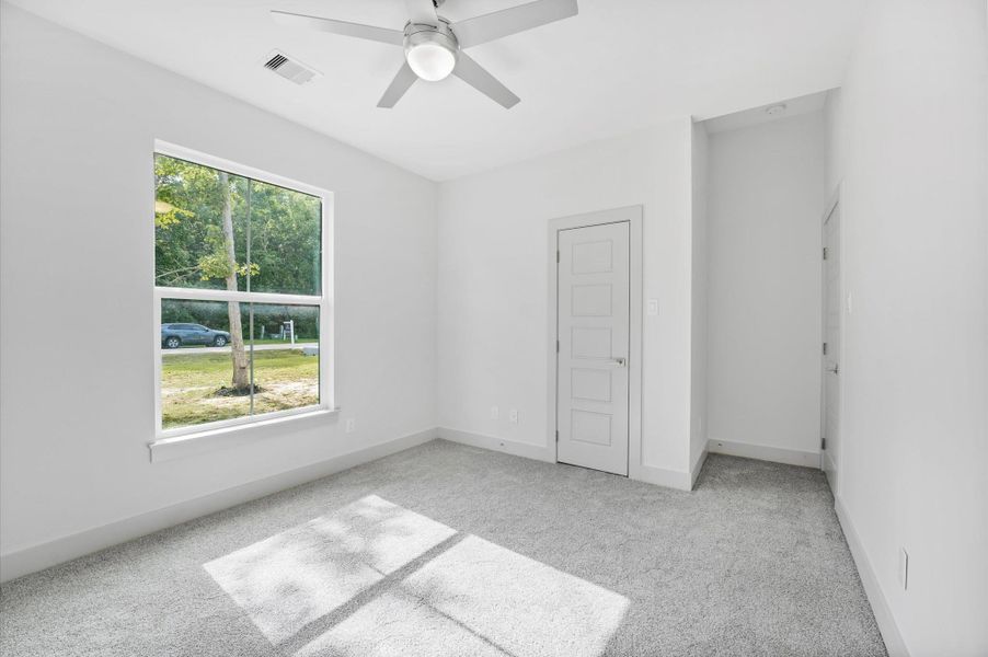 Bright and inviting bedroom with neutral walls and carpet, featuring a large window for natural light, a ceiling fan, and a modern door. Bright and inviting bedroom with neutral walls and carpet, featuring a large window for natural light, a ceiling fan, and a modern door.