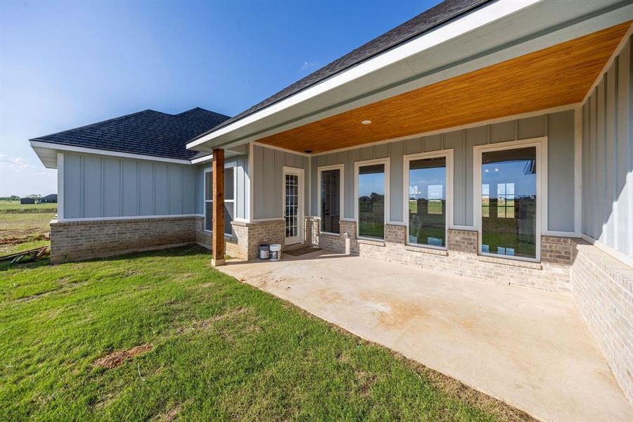 Rear view of property with board and batten siding, brick siding, a yard, roof with shingles, and a patio Rear view of property with board and batten siding, brick siding, a yard, roof with shingles, and a patio