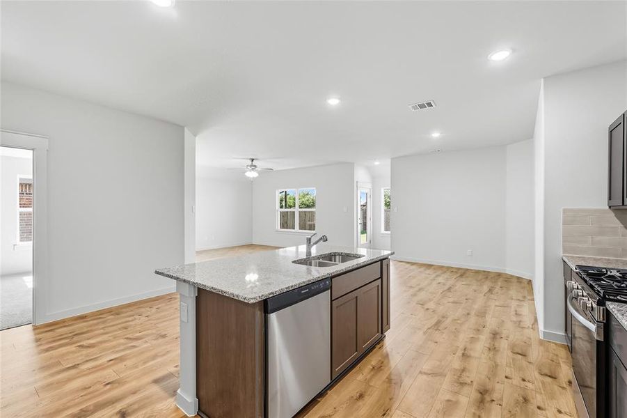 Kitchen featuring appliances with stainless steel finishes, light stone countertops, recessed lighting, open floor plan, and a center island with sink