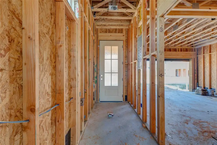 Interior entry view showing framed walls, exposed wiring, electrical panel placement, and a door leading toward the exterior or garage area. This construction-stage photo provides a close look at the home’s build progress and layout, capturing the transition between entry, garage, and main living spaces before drywall and finish selections are installed. Interior entry view showing framed walls, exposed wiring, electrical panel placement, and a door leading toward the exterior or garage area. This construction-stage photo provides a close look at the home’s build progress and layout, capturing the transition between entry, garage, and main living spaces before drywall and finish selections are installed.