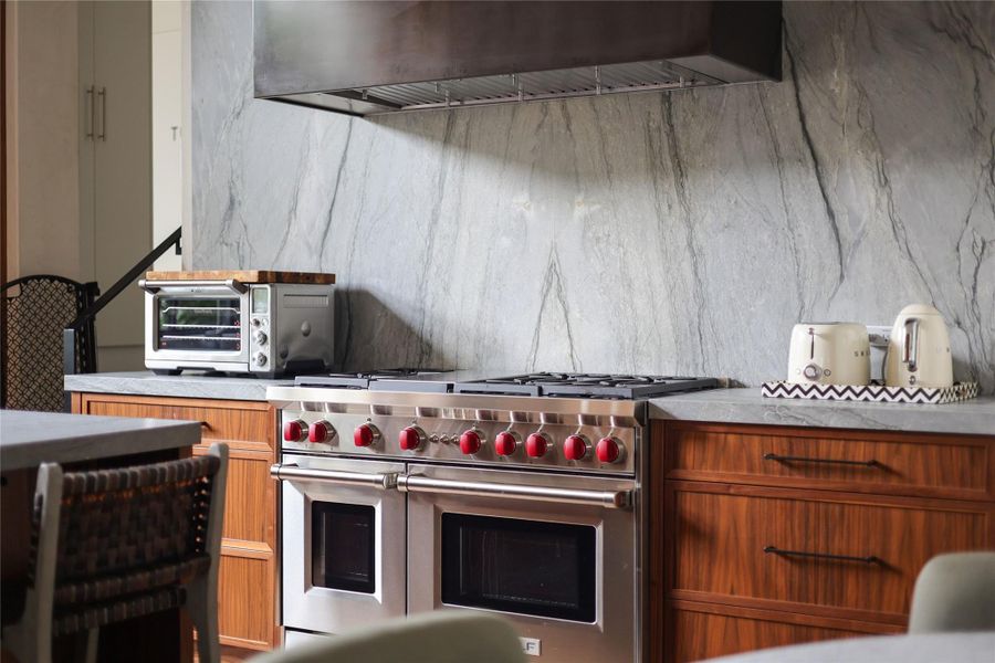 A gourmet kitchen features rich walnut cabinetry, and a striking leathered quartzite stone backsplash.