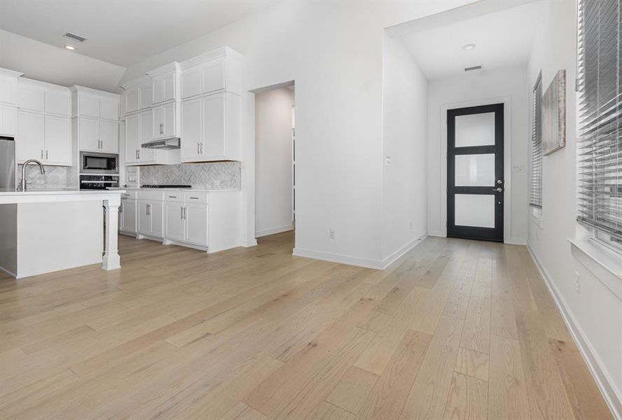 Kitchen with white cabinetry, decorative backsplash, light wood-style flooring, a kitchen bar, and appliances with stainless steel finishes Kitchen with white cabinetry, decorative backsplash, light wood-style flooring, a kitchen bar, and appliances with stainless steel finishes