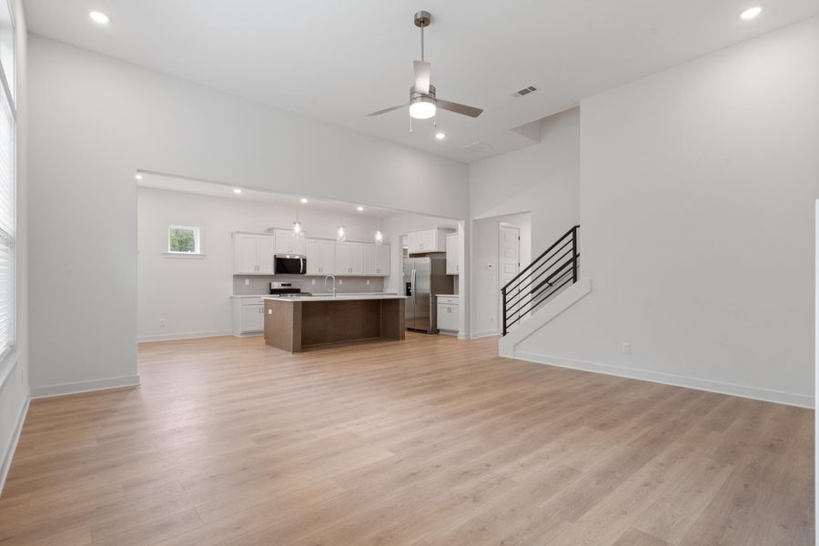 Vaulted ceilings with recessed lighting and a ceiling fan, wood-finish flooring, a kitchen with stainless steel appliances, a center island with pendant lighting, and a staircase featuring a metal railing Vaulted ceilings with recessed lighting and a ceiling fan, wood-finish flooring, a kitchen with stainless steel appliances, a center island with pendant lighting, and a staircase featuring a metal railing