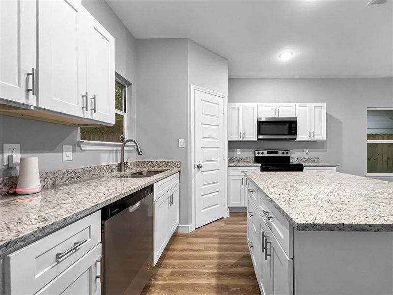 Kitchen with appliances with stainless steel finishes, wood finished floors, white cabinetry, light stone counters, and a center island