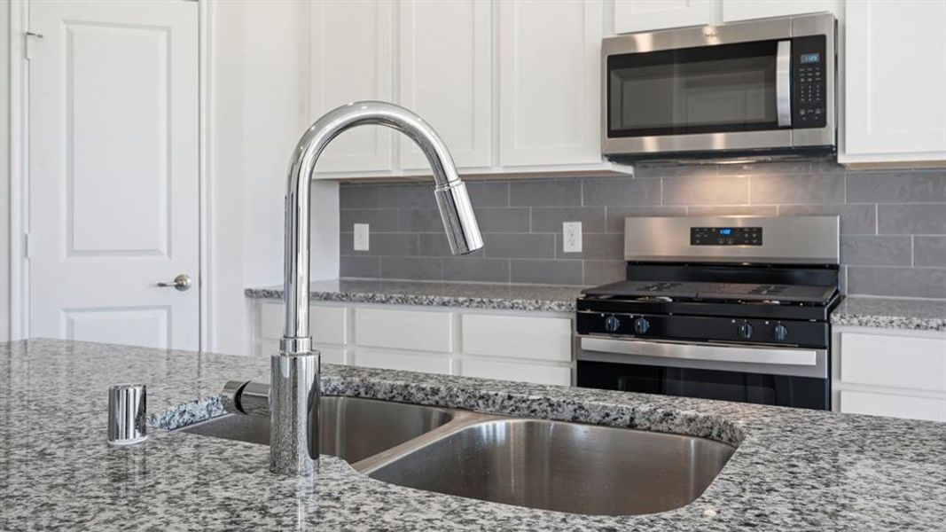 Kitchen with stainless steel appliances, light stone countertops, white cabinets, and backsplash Kitchen with stainless steel appliances, light stone countertops, white cabinets, and backsplash