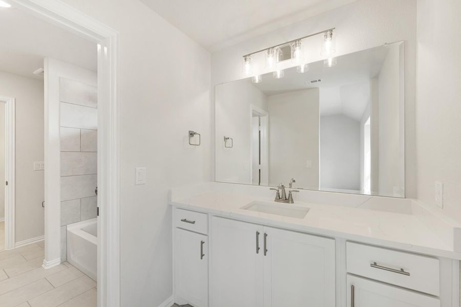 Bathroom with white vanity, quartz countertop, large mirror, and soaking tub visible in background