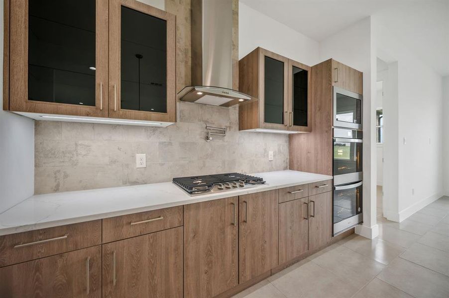 Kitchen featuring wall chimney range hood, decorative backsplash, stainless steel gas stovetop, and double oven Kitchen featuring wall chimney range hood, decorative backsplash, stainless steel gas stovetop, and double oven