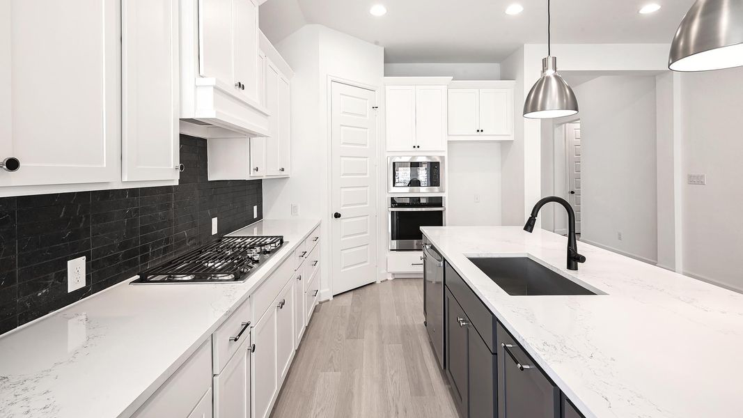 Kitchen with light wood-style flooring, white cabinets, light stone counters, appliances with stainless steel finishes, and hanging light fixtures Kitchen with light wood-style flooring, white cabinets, light stone counters, appliances with stainless steel finishes, and hanging light fixtures